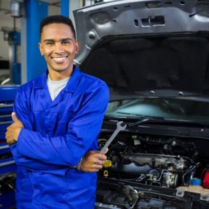 A skilled mechanic stands next to a car with a confident smile, representing the expertise gained through the Certificate IV in Automotive Electrical Technology at Sheffield College, where students acquire specialized skills in automotive electrical systems. This program empowers students to confidently diagnose and repair electrical components, ensuring optimal performance and reliability of vehicles.