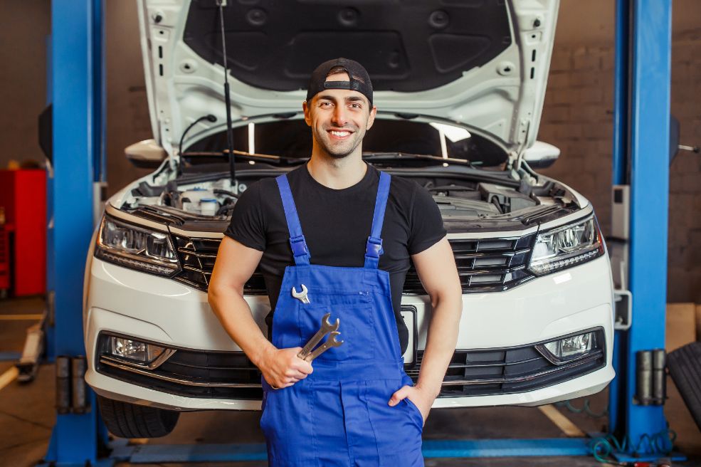 A mechanic wearing a blue uniform intently works on a car engine in a well-equipped workshop.