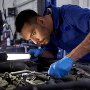 A mechanic in a blue uniform meticulously examines a car in a well-equipped workshop. The mechanic's focus is on the engine components while utilizing specialized tools for diagnosis and inspection. The image represents the dedication and expertise gained through the Certificate III in Light Vehicle Mechanical Technology at Sheffield College, providing students with the skills required for professional maintenance and repair of light vehicles.